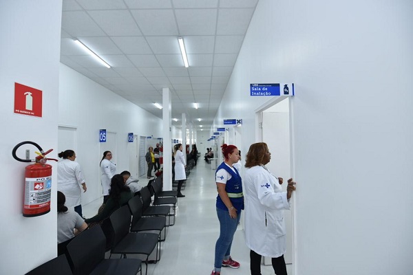 #PraCegoVer: Foto da parte interna da unidade, com munícipes e funcionários do local. Algumas pessoas estão sentadas nas cadeiras de espera e outras estão ao fundo.